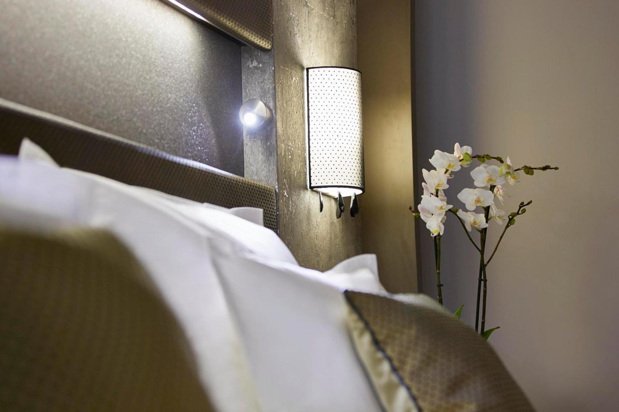 Steigenberger Hotel Am Kanzleramt Berlin Bilik gambar The photo displays a cozy bedroom scene. In the foreground, there are neatly arranged white pillows on a bed, suggesting comfort. A stylish wall sconce is mounted on the headboard, providing soft lighting. To the side of the bed, there is a decorativ